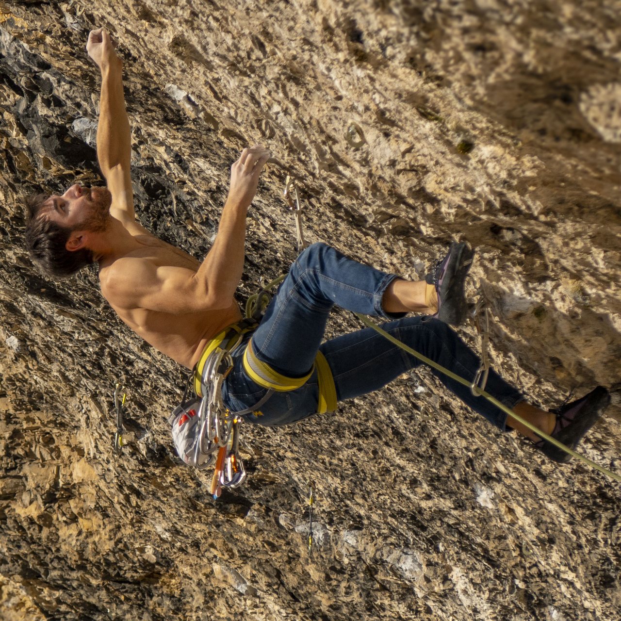 Armin Buchroithner mid-move on a steep limestone wall, roped, one arm reaching.