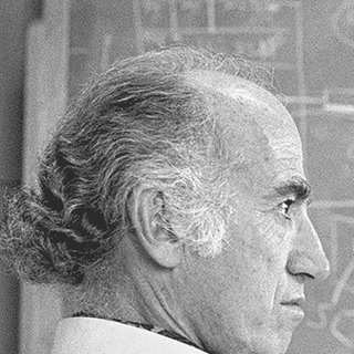Jonas Salk in profile, seated at a blackboard covered in diagrams.