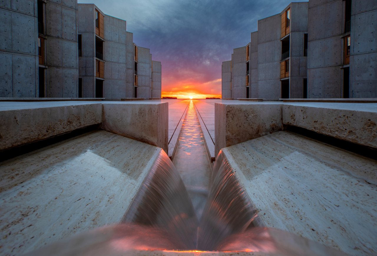 The Salk Institute courtyard at sunset, its central water channel running between the concrete towers toward the Pacific.